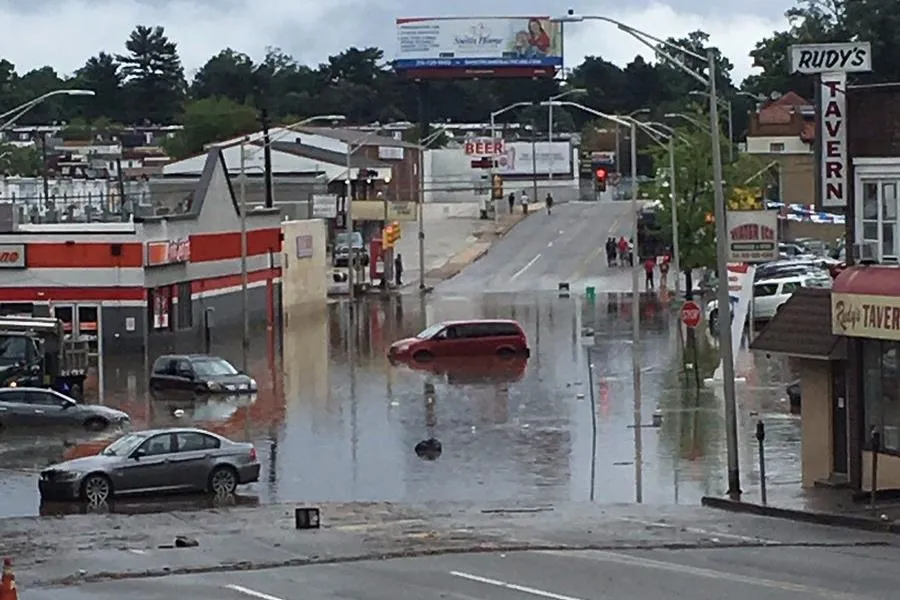 An image of several cars partially underwater on a flooded roadway with businesses on either side.
